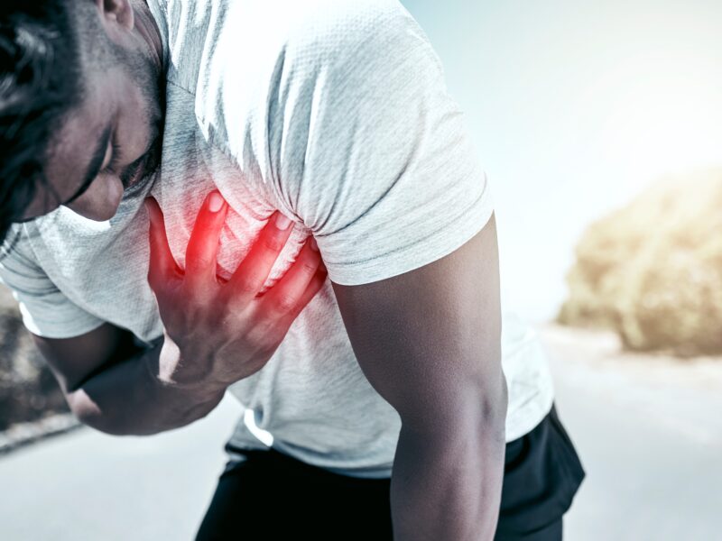 Man in white t-shirt leans over while clutching his chest from pain due to arrhythmia.