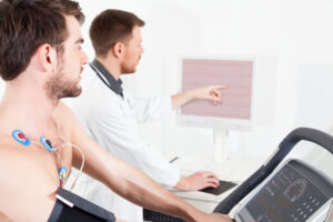 A young man undergoes a cardiac stress test on a treadmill while a doctor monitors