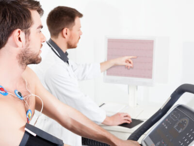 A young man undergoes a cardiac stress test on a treadmill while a doctor monitors