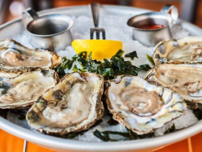 Delicious, fresh-shucked oysters in half shells sit on a chilled platter with a lemon garnish forked in the middle.