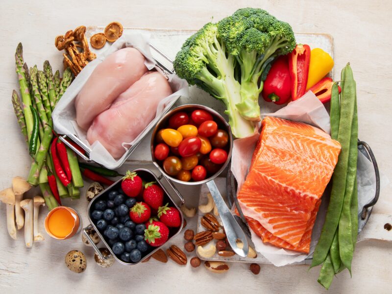 Various healthy heart food; vegetables, nuts, and proteins laid out on off-white background