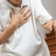 An elderly man in a white polo tee is suffering COPD symptoms while clutching his chest.